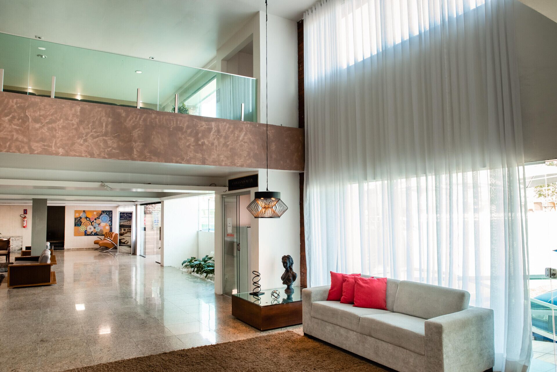A spacious lobby with a high ceiling, a glass railing on the upper level, and a large window with sheer curtains.