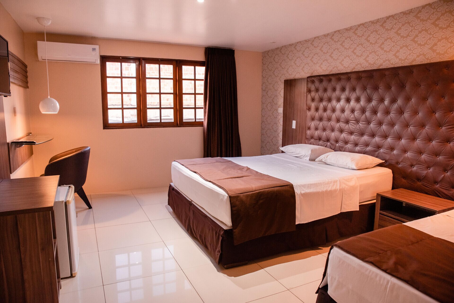 Una habitación de hotel con cama, escritorio, silla y ventana con cortinas.