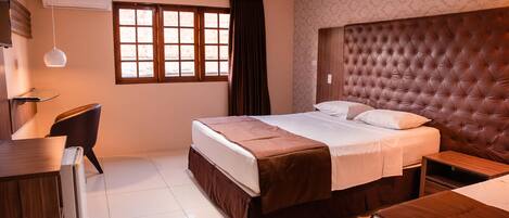 Una habitación de hotel con cama, escritorio, silla y ventana con cortinas.