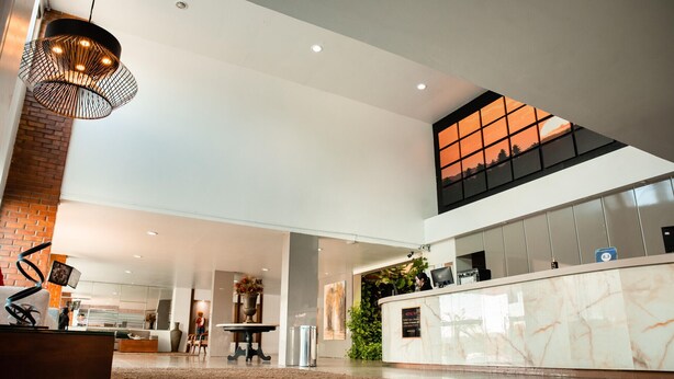 A spacious lobby with a reception desk, a large chandelier, and a view of the sky through a window. - Hotel Village Premium Caruaru (Caruaru)