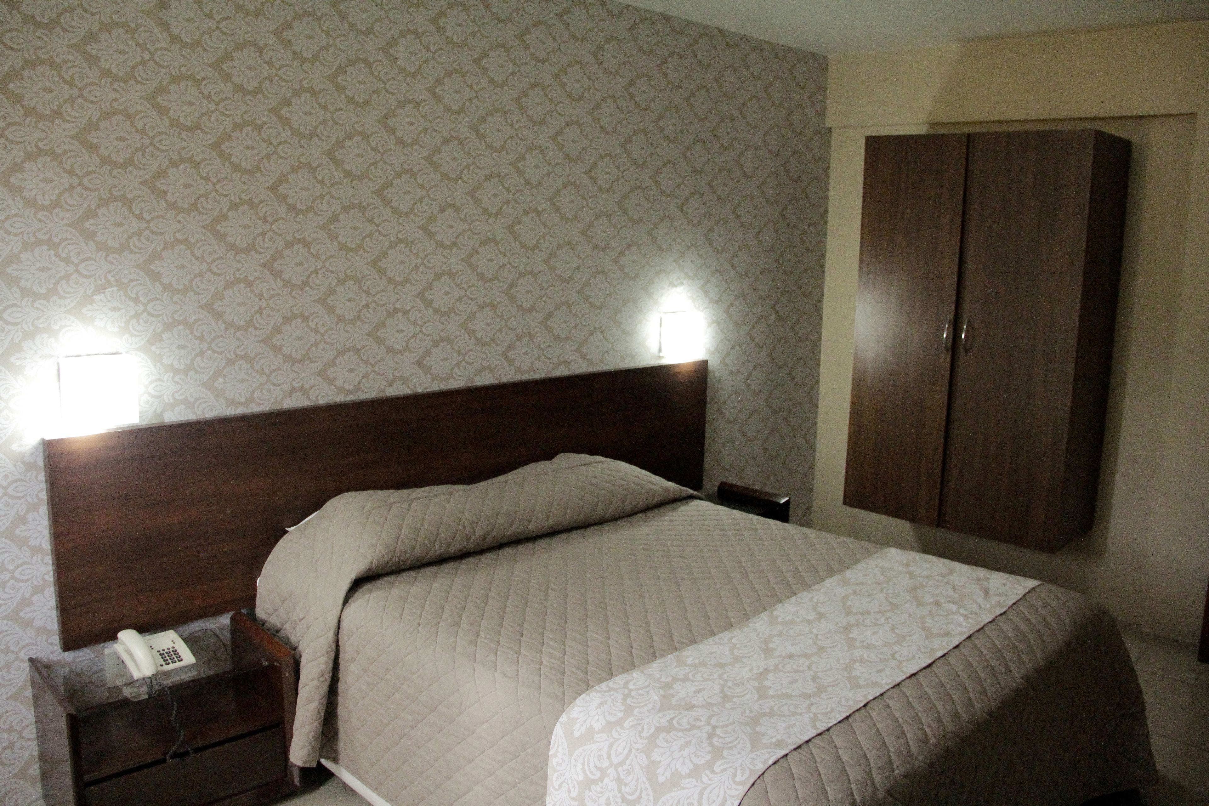 A bedroom with a double bed, a nightstand with a phone, and a wardrobe.
