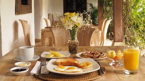 Ein Frühstückstisch mit Holzplatte, eine Blumenvase und verschiedene Frühstücksleckereien, darunter Toast, Eier und Obst.