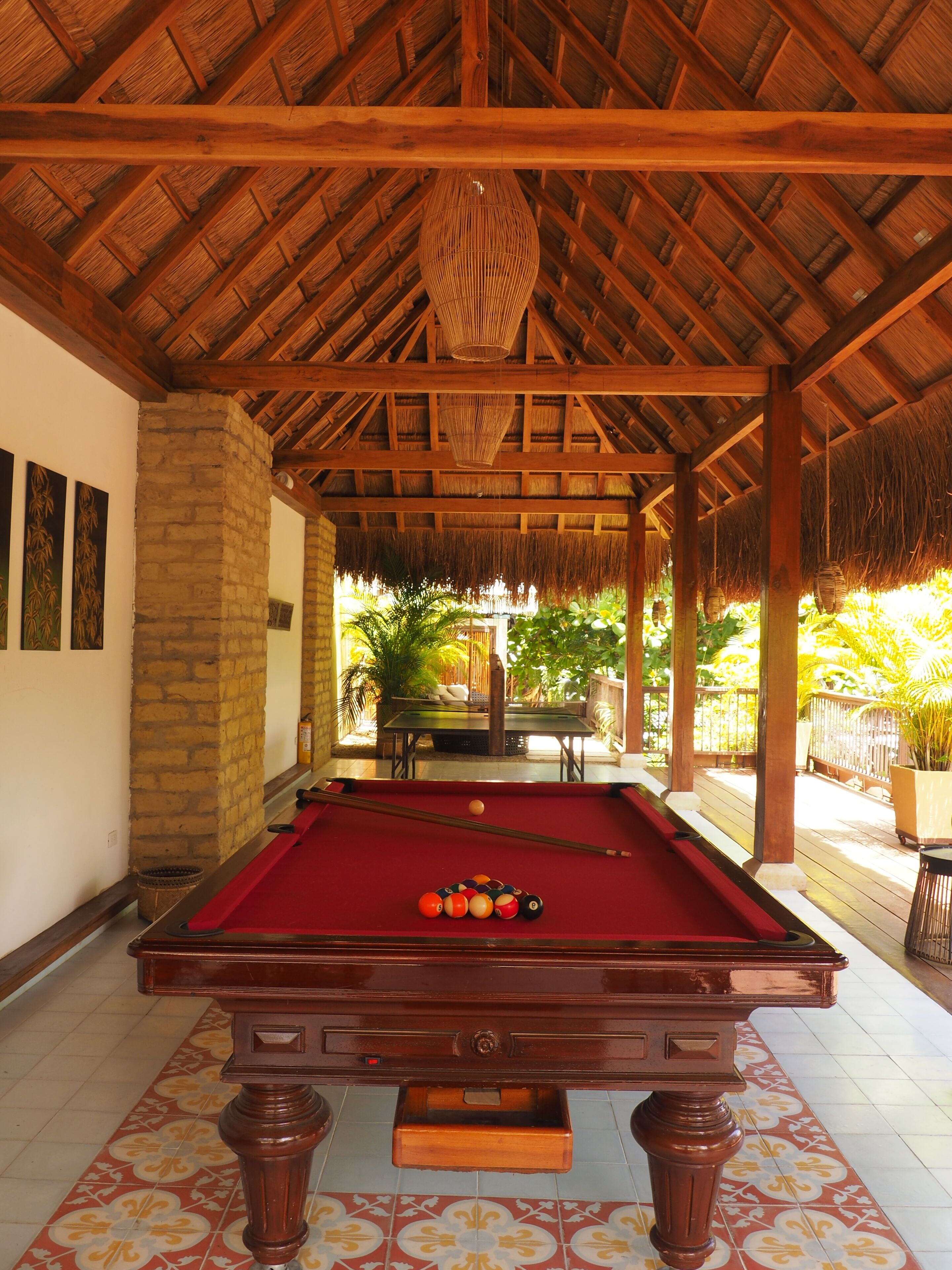 A pool table with balls, a brick pillar, and a thatched roof structure.