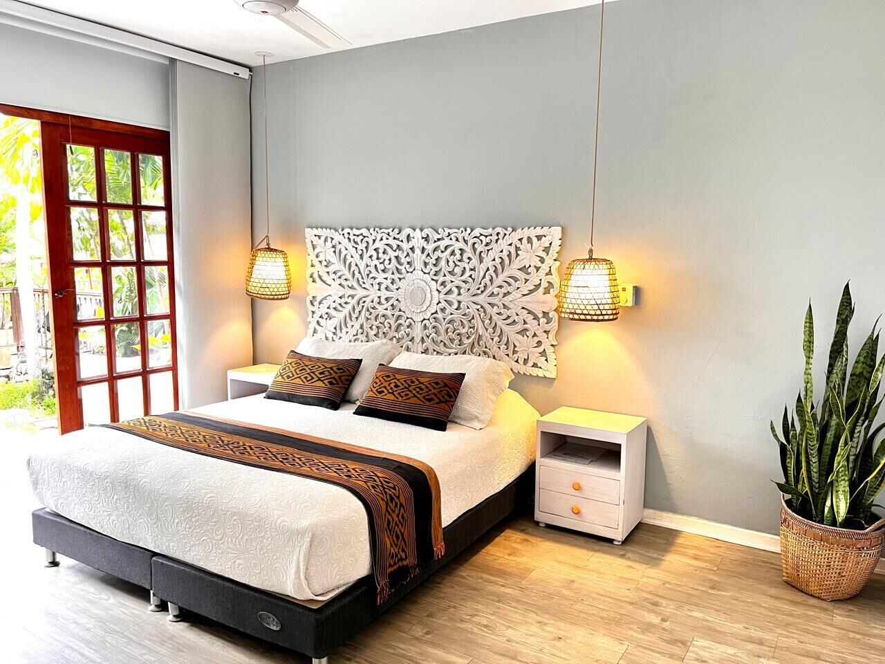 Un dormitorio moderno con una cama grande, decoración en la pared, lámparas de noche, una mesita de noche y una planta en maceta.