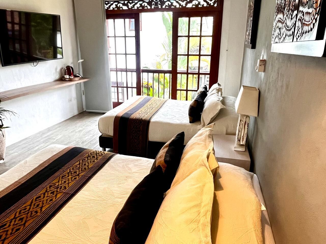 A hotel room with two beds, a TV, a window with a view, and a shelf with a plant.