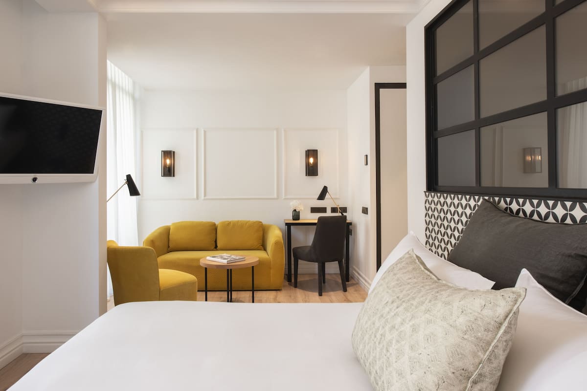 A modern hotel room with a large bed, a sofa, a desk, and a TV mounted on the wall.