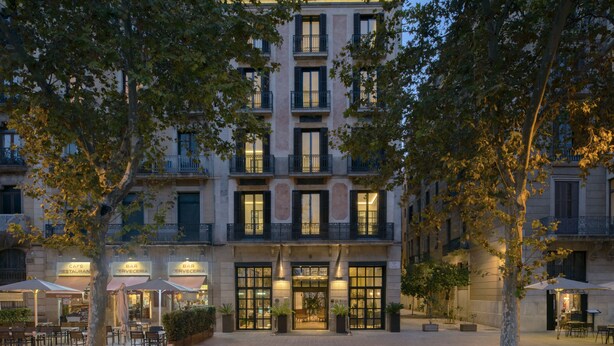 A multi-story building with a courtyard, featuring outdoor seating areas and signage for a cafe and bars. - Serras Barcelona (Barcelona)