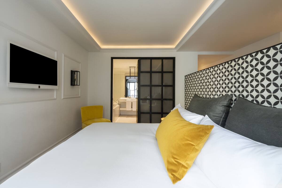 A modern hotel room with a large bed, a flat-screen TV mounted on the wall, and a sliding door leading to a bathroom.