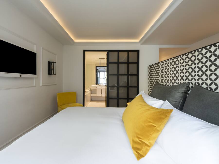Una camera d'albergo moderna con un letto grande, una TV a schermo piatto montata a parete e una porta scorrevole che dà su un bagno.