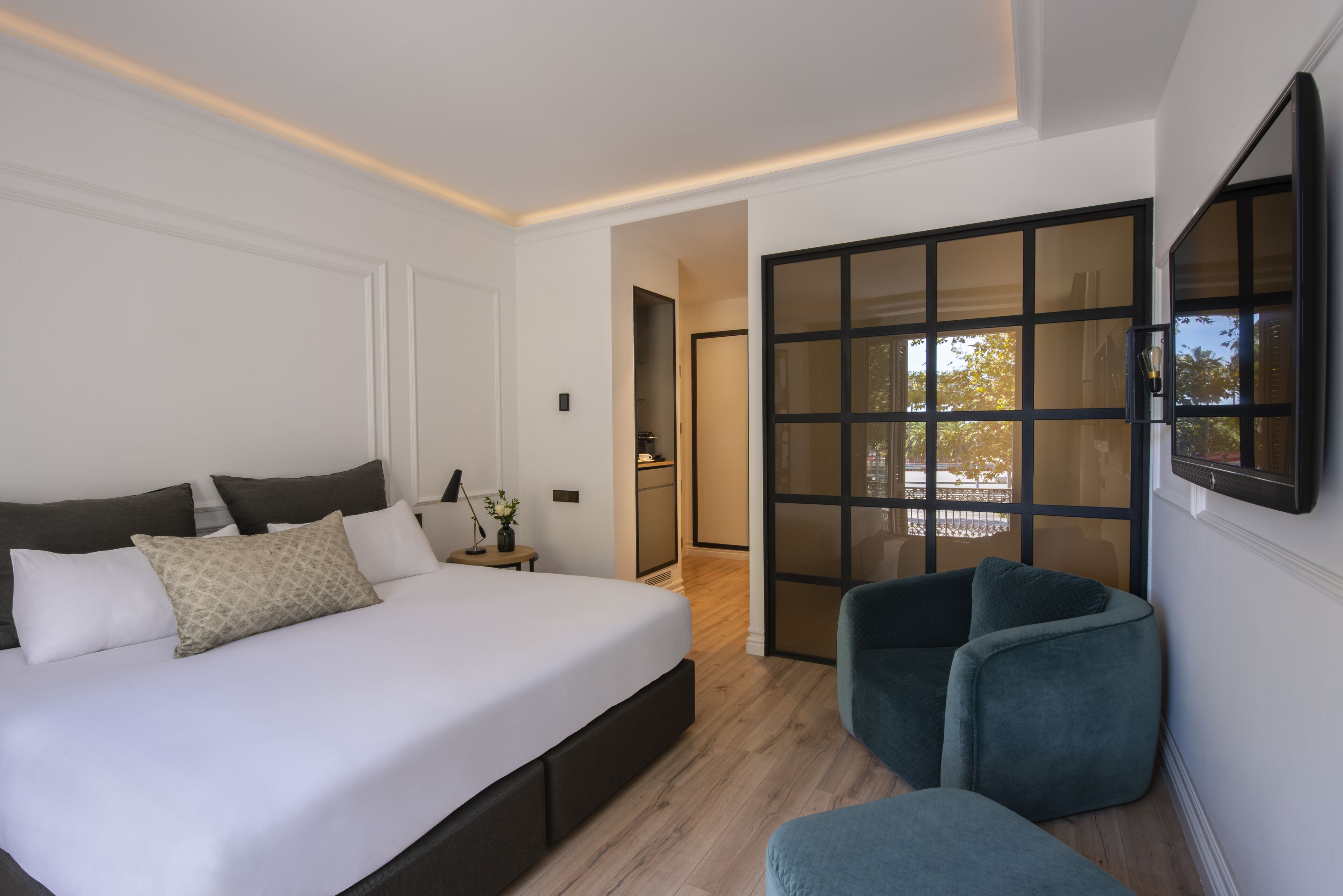 A modern bedroom with a large bed, a seating area, and a sliding glass door leading to a balcony.