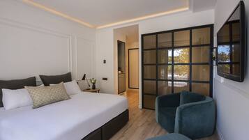 A modern bedroom with a large bed, a seating area, and a sliding glass door leading to a balcony.