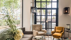 A modern living room with a sofa, armchair, and ottoman, a glass coffee table, and a large window with a view of palm trees. - Serras Barcelona (Barcelona)