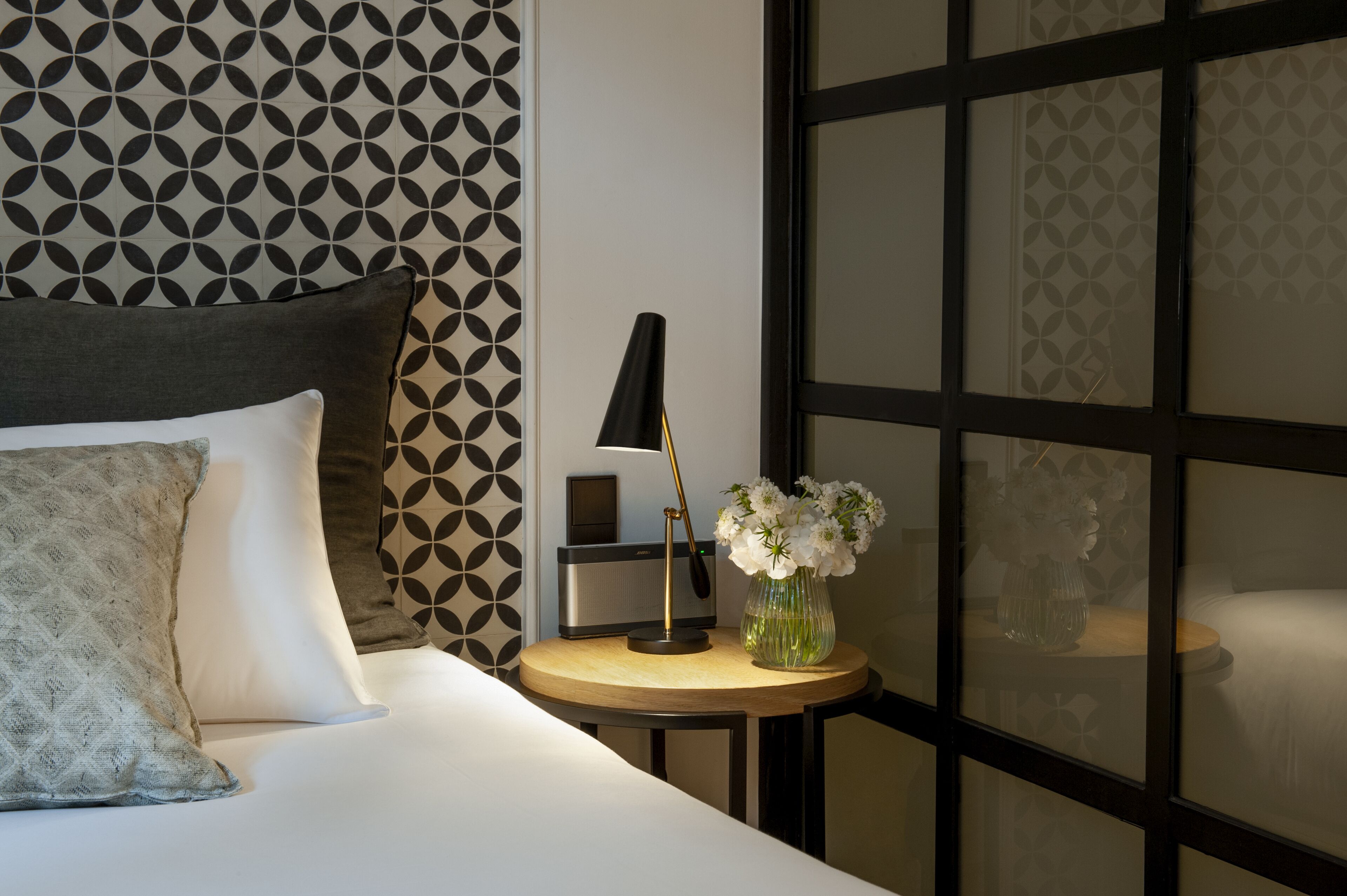 A neatly made bed with pillows, a bedside table with a lamp, and a vase with flowers.