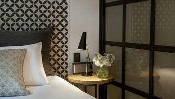 A neatly made bed with pillows, a bedside table with a lamp, and a vase with flowers.