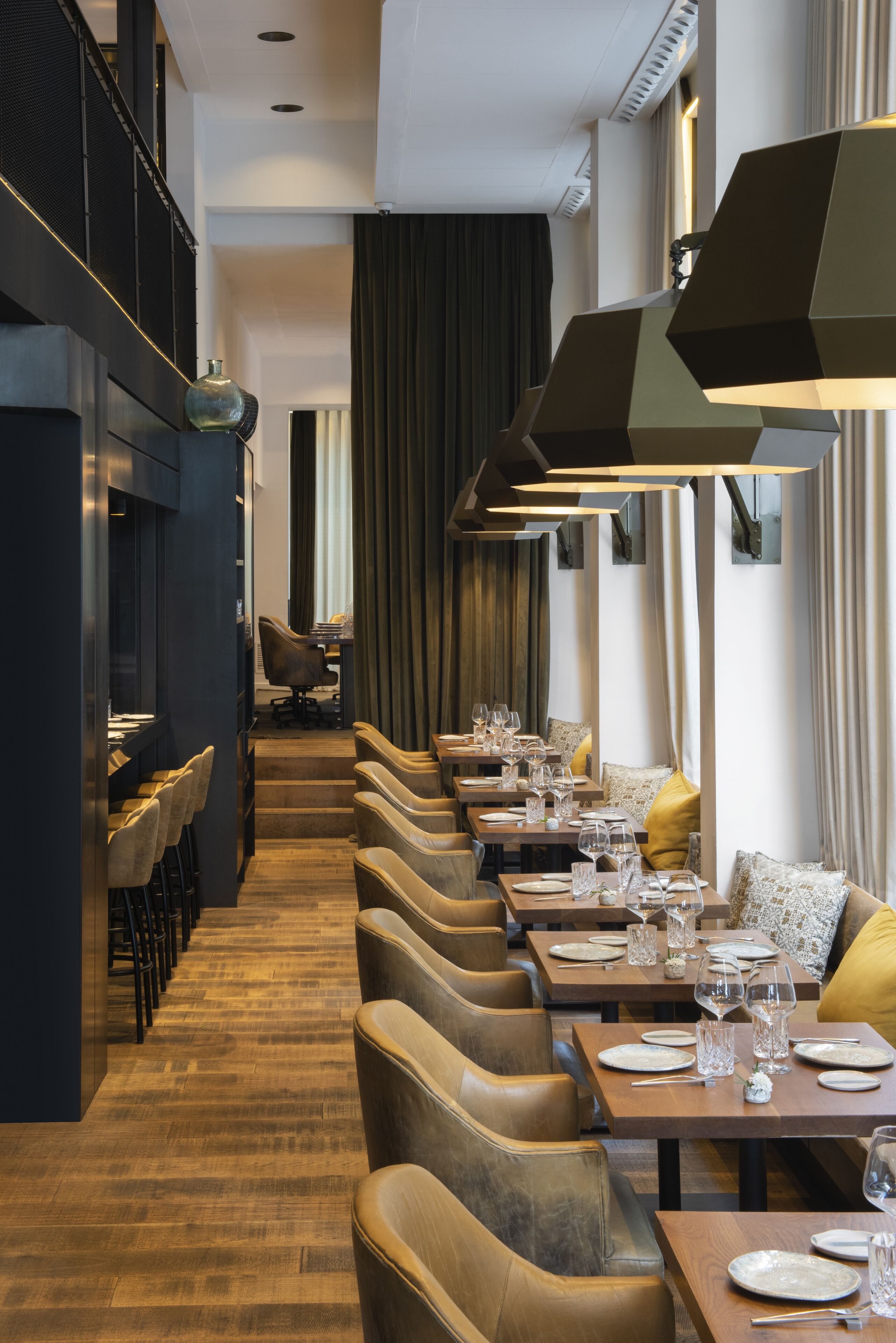 A modern restaurant interior with a long counter, multiple tables, and chairs.