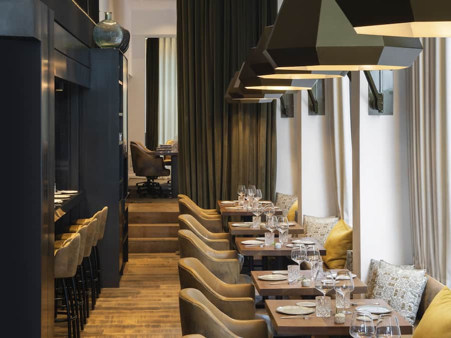 A modern restaurant interior with a long counter, multiple tables, and chairs.