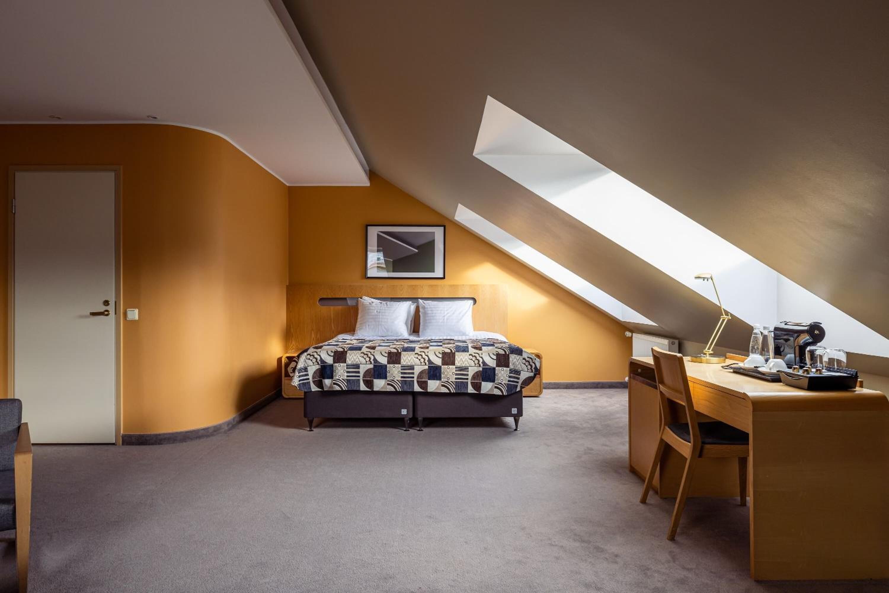 Une chambre aménagée dans les combles, avec un lit, un bureau et une fenêtre de toit.