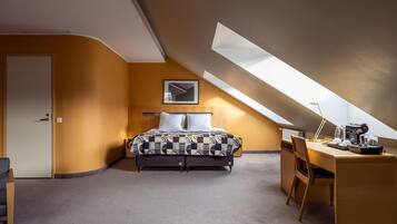 An attic bedroom with a bed, desk, and skylight.