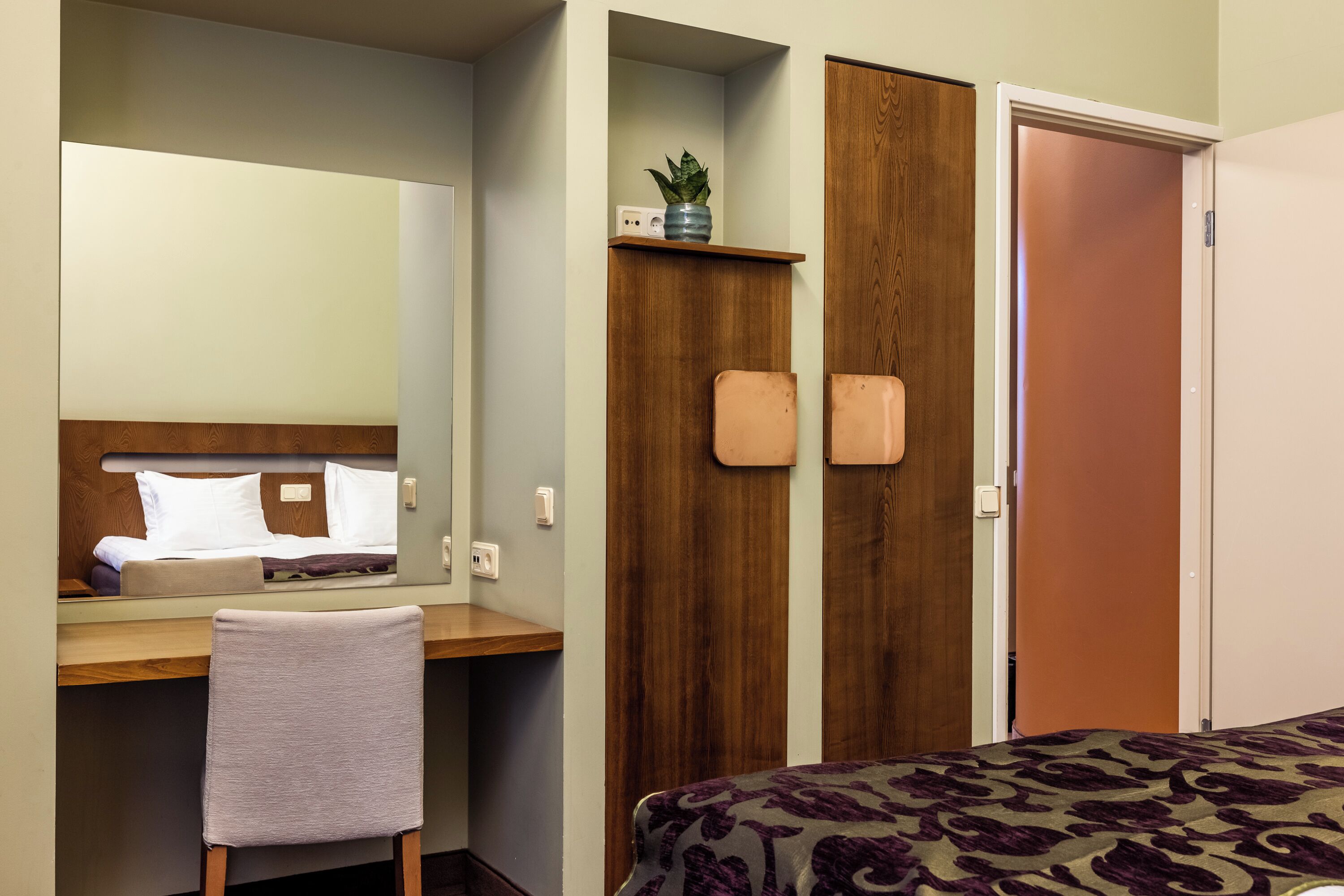 Une chambre d’hôtel comprenant un lit, un bureau avec une chaise, un miroir, une armoire et une porte.