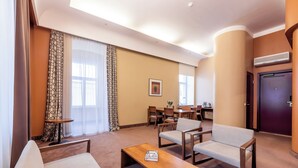 A hotel room with a sofa, a wooden coffee table, a dining area with chairs and a table, and a door. - Hotel London Tartu (Tartu)