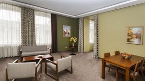 A living room with a sofa, chairs, a coffee table, a dining table with chairs, a vase with flowers, and two paintings on the walls. - Hotel London Tartu (Tartu)