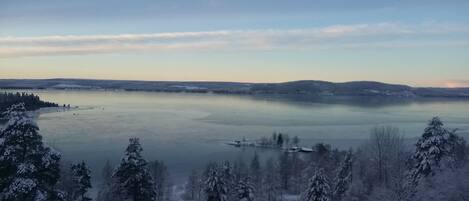 A panoramic view of a lake surrounded by snow-covered trees and distant hills.