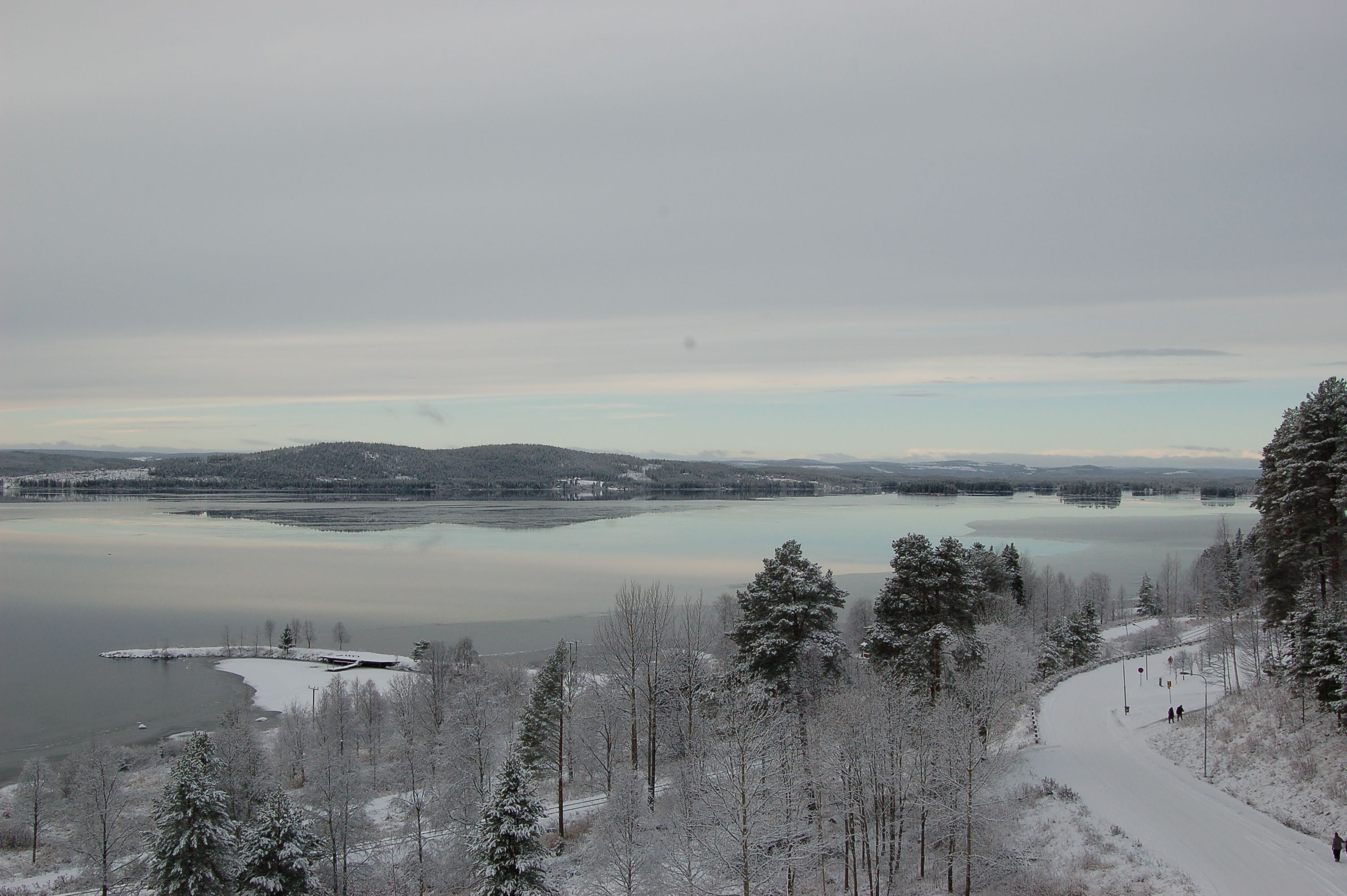Un paysage hivernal avec un lac, des arbres couverts de neige et un ciel dégagé.