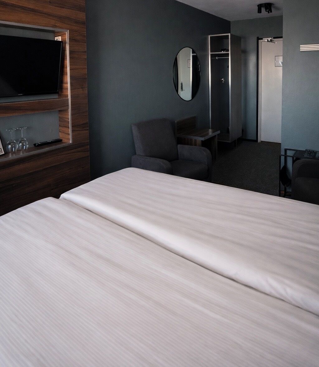 Una habitación de hotel con una cama grande, televisión, espejo, una silla y un escritorio.