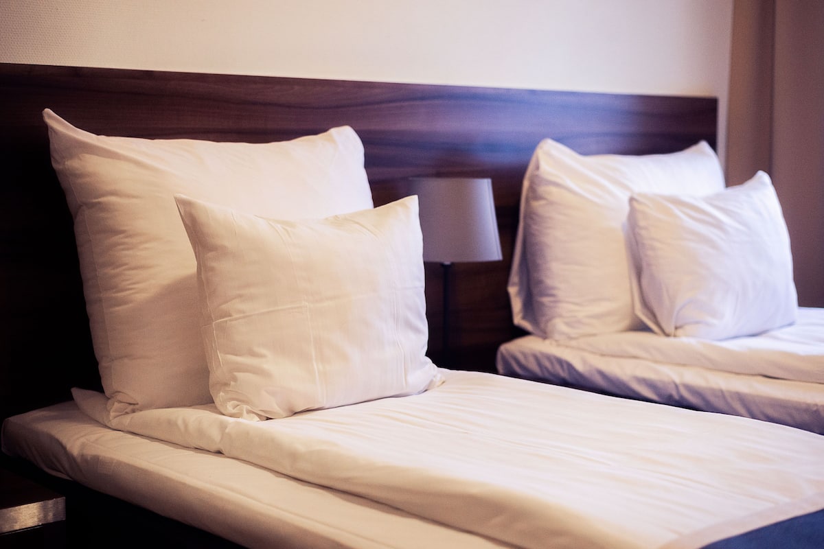 Habitación de hotel con dos camas, cada una con ropa de cama y almohadas blancas.