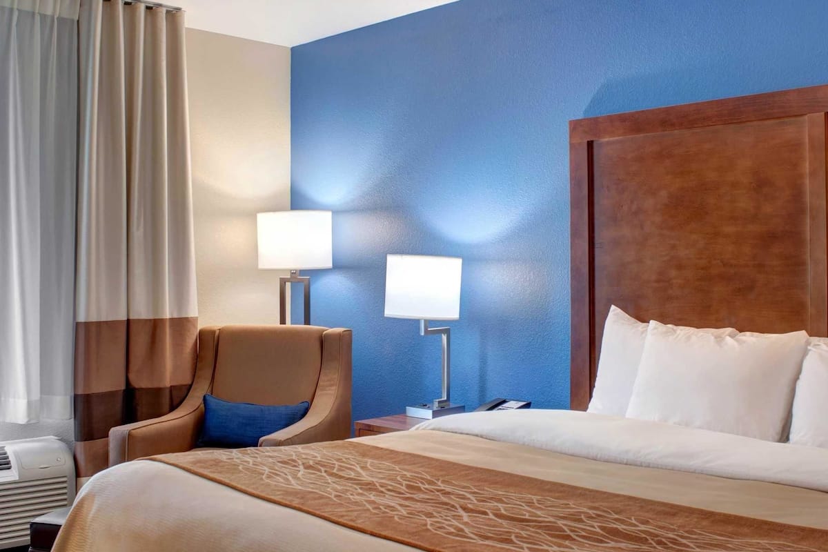 A hotel room with a large bed, a chair, two bedside lamps, a nightstand, and a window with curtains.
