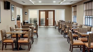 A spacious dining area with multiple tables and chairs, a large door with frosted glass panels, and a view through the door.