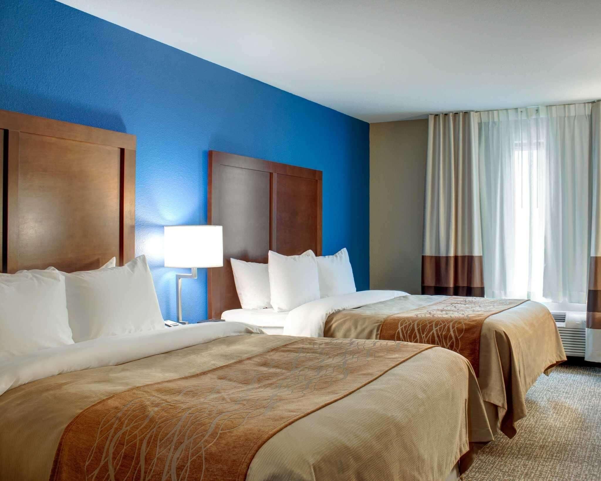 Een hotelkamer met twee bedden, een nachtkastje, een lamp en een raam met gordijnen.