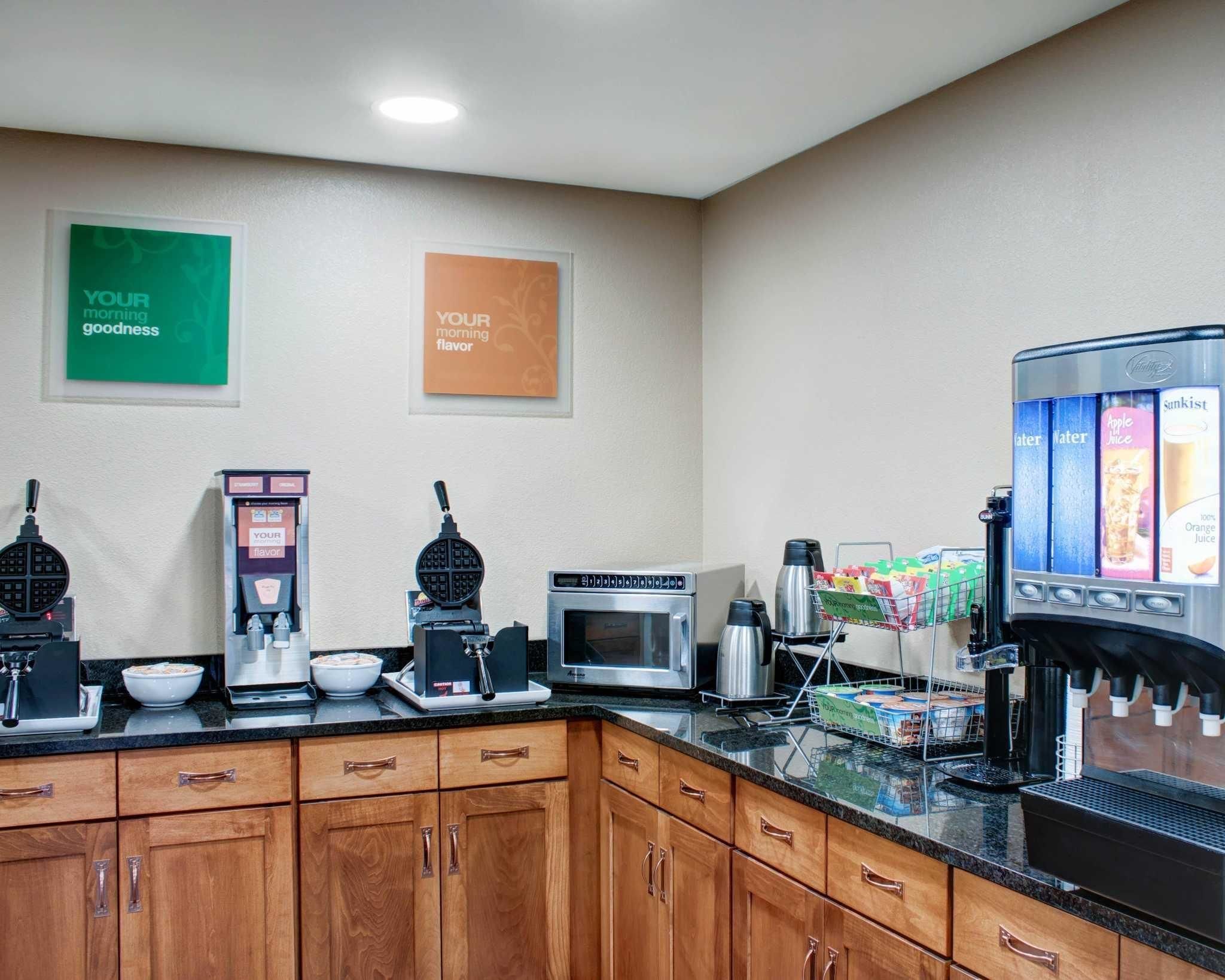 Una cocina equipada con una plancha para gofres, cafetera, microondas y dispensador de bebidas.