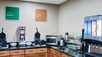 Una cocina equipada con una plancha para gofres, cafetera, microondas y dispensador de bebidas.