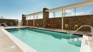 A swimming pool with a stone wall and a covered seating area with chairs. - Home2 Suites by Hilton Midland (Midland)