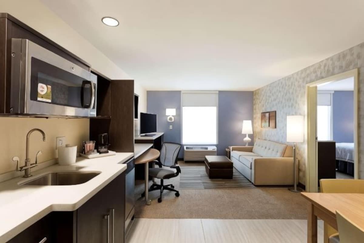 A modern hotel room with a kitchenette, a sofa, a desk, and a bed.
