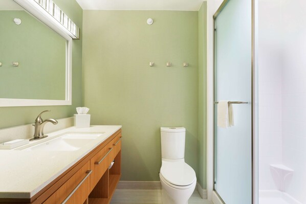 A bathroom with a double sink, wooden vanity, toilet, and a glass shower enclosure. - Home2 Suites by Hilton Midland (Midland)