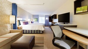 A hotel room with a bed, a desk, a chair, a TV, and a bookshelf. - Home2 Suites by Hilton Midland (Midland)