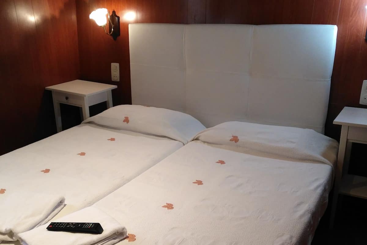 A neatly made bed with white bedding and a remote control on it. There are two nightstands, one on each side of the bed, and a wall-mounted light fixture above the bed.