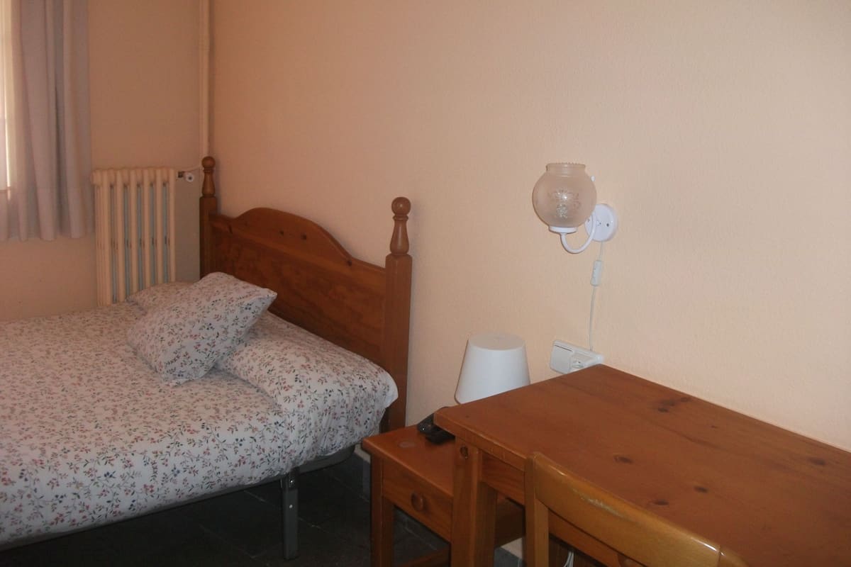 A single bed with a wooden headboard, a bedside table, a lamp, and a radiator.