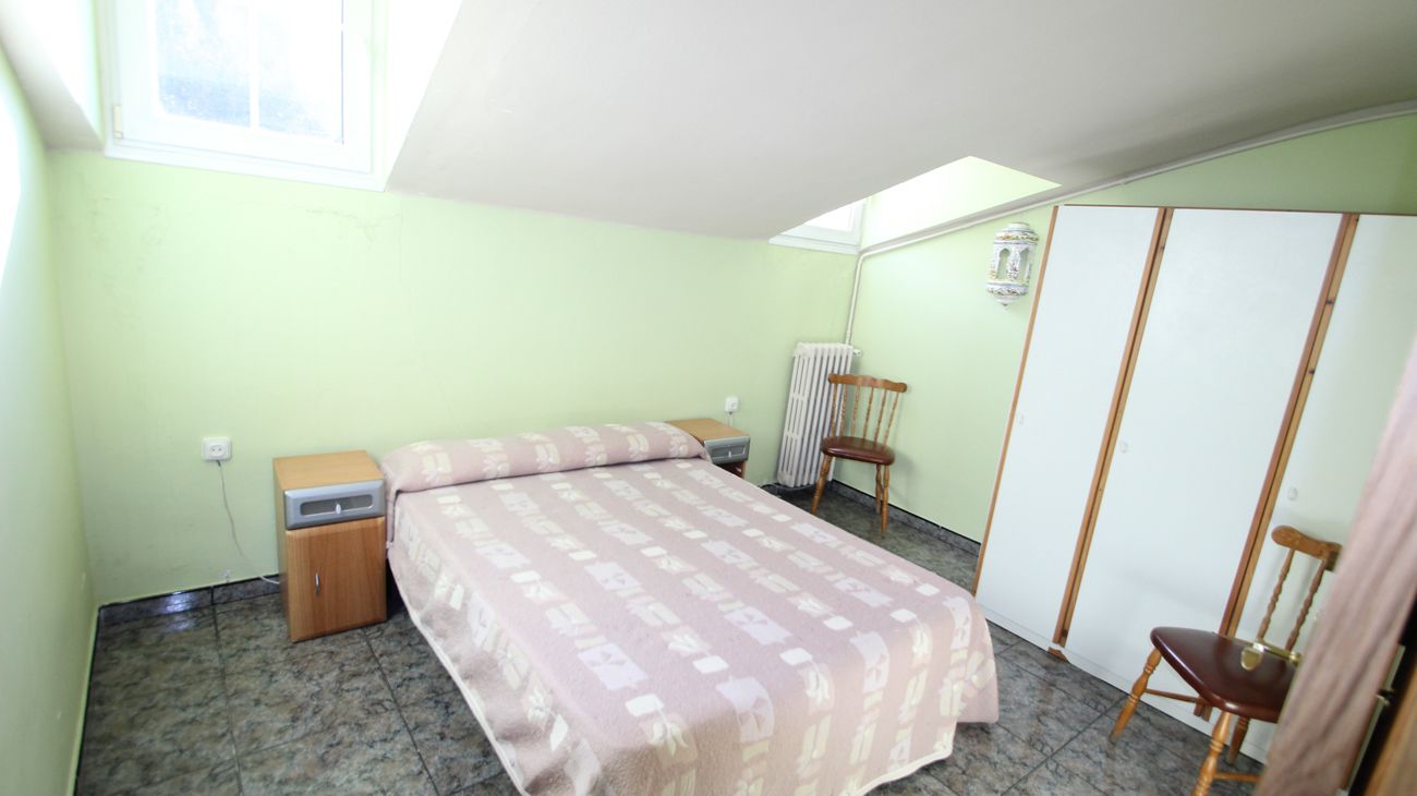 A small, well-lit bedroom with a bed, a nightstand, a radiator, and a wardrobe.