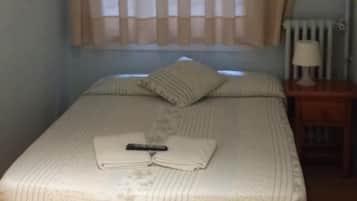 Een enkel bed met een deken en kussens, een nachtkastje met een lamp, en een raam met gordijnen.