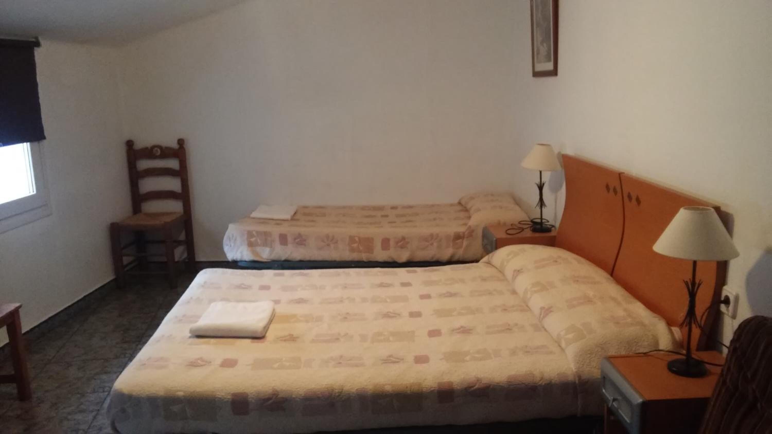 Una habitación sencilla con dos camas, una silla, un escritorio y una lámpara.