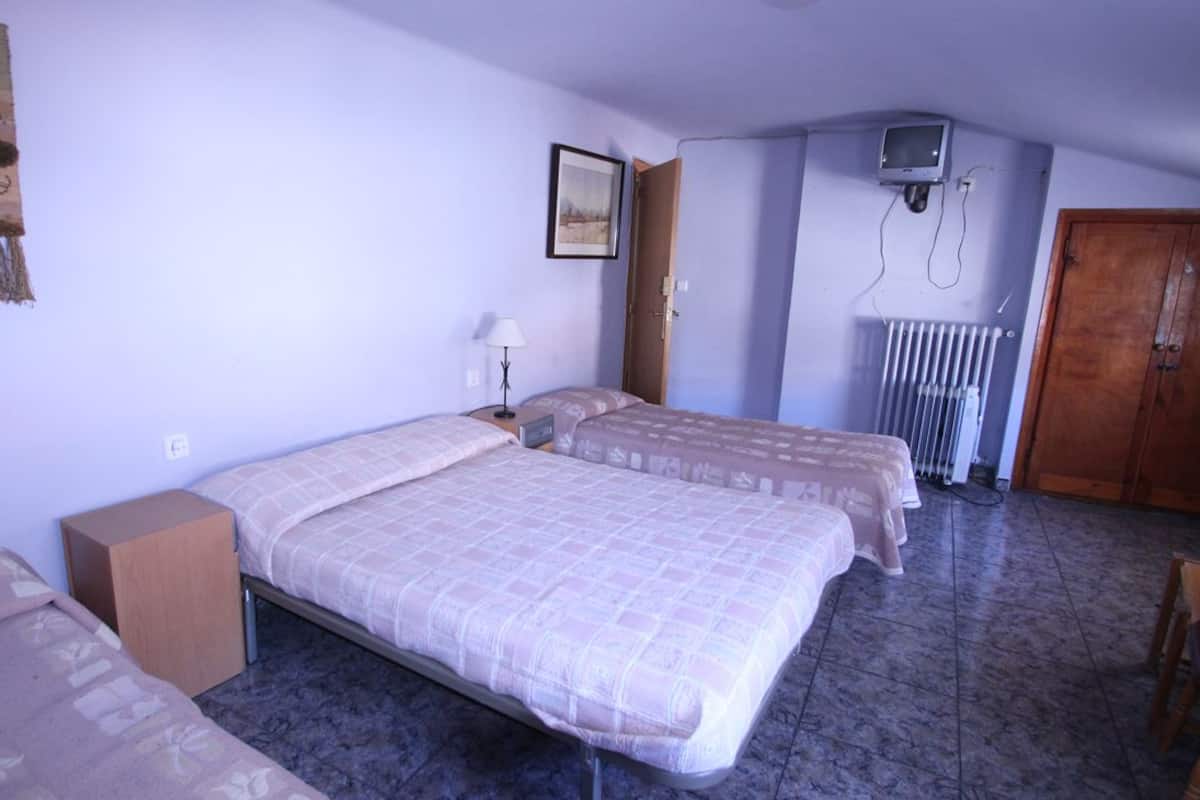 A room with two beds, a wooden wardrobe, a radiator, and a television on the wall.