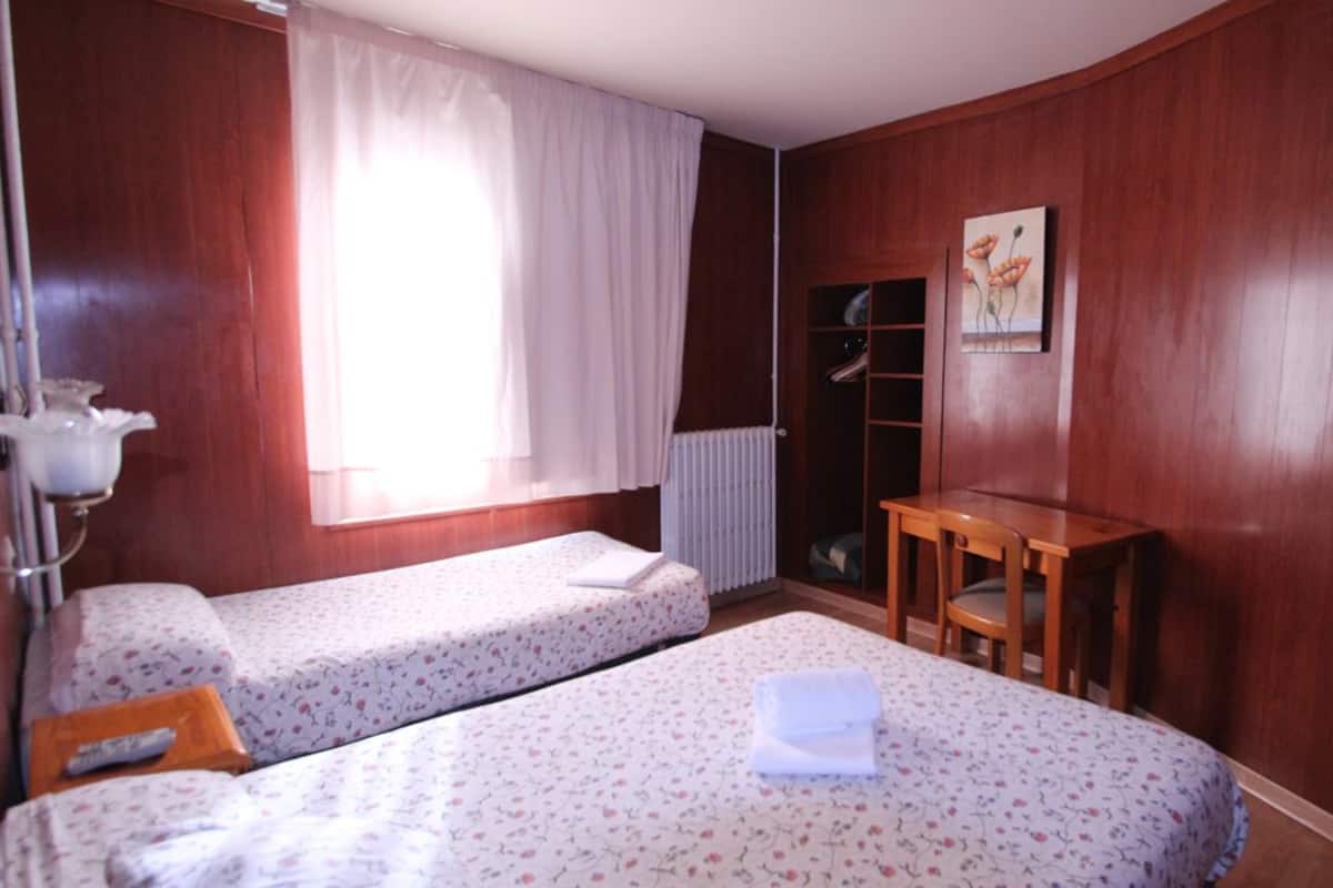 A room with two single beds, a wooden table, a radiator, and a wardrobe.