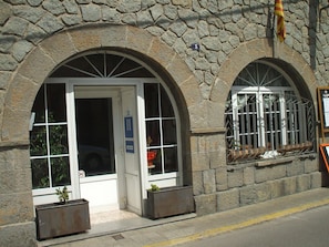 Un edificio de piedra con dos portales arqueados, cada uno con un ventanal. Hay carteles que indican un restaurante y un hotel.