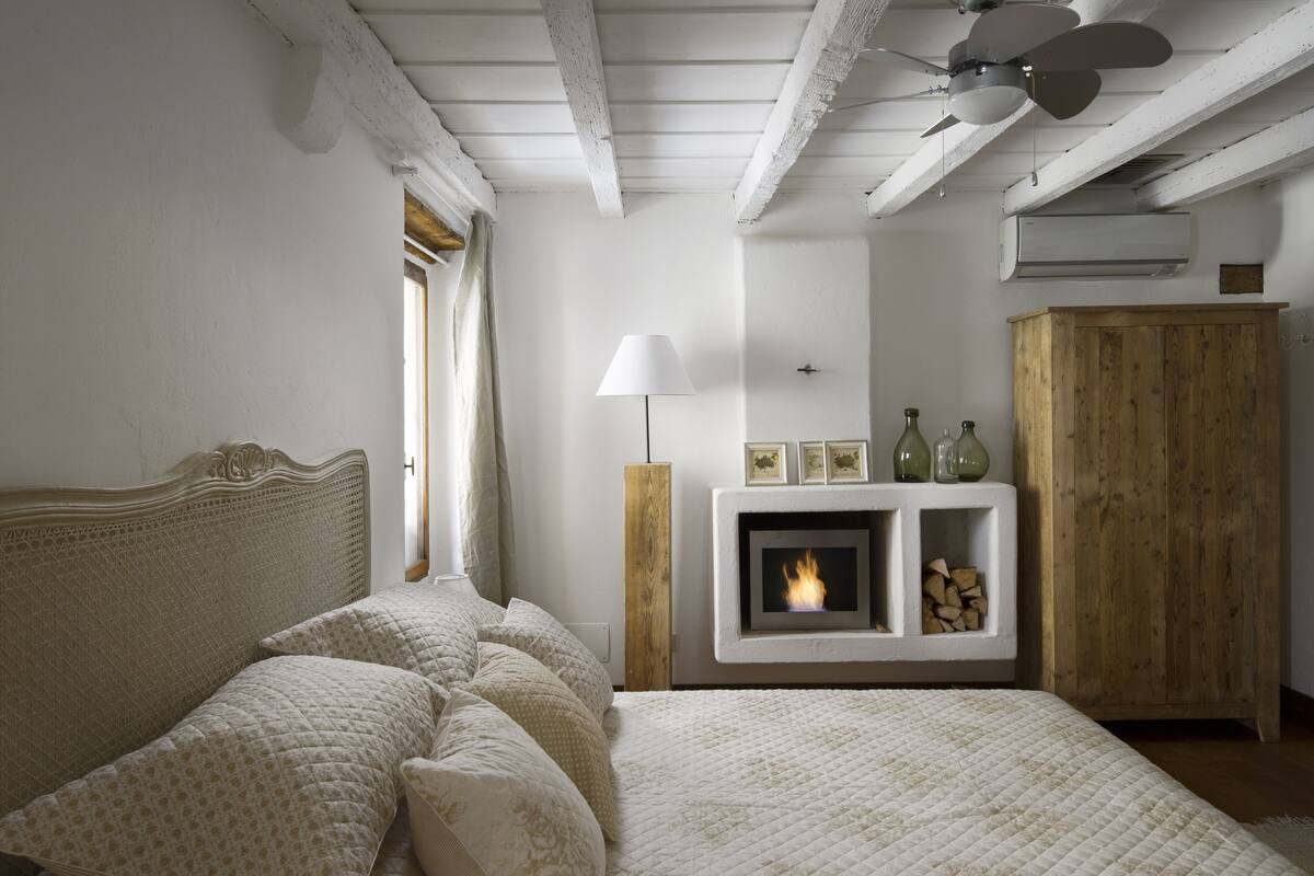 A bedroom with a bed, a fireplace, a wooden wardrobe, and a ceiling fan.