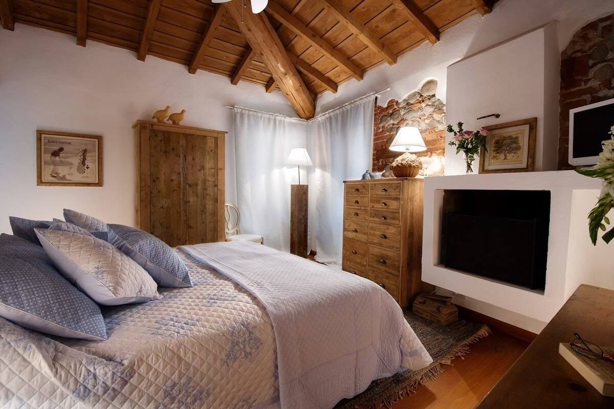 A bedroom with a bed, wooden wardrobe, a television, and a stone wall.