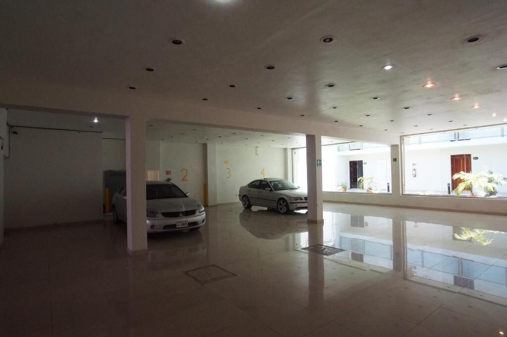 Amplio espacio interior con suelo pulido, varias puertas y dos coches estacionados.