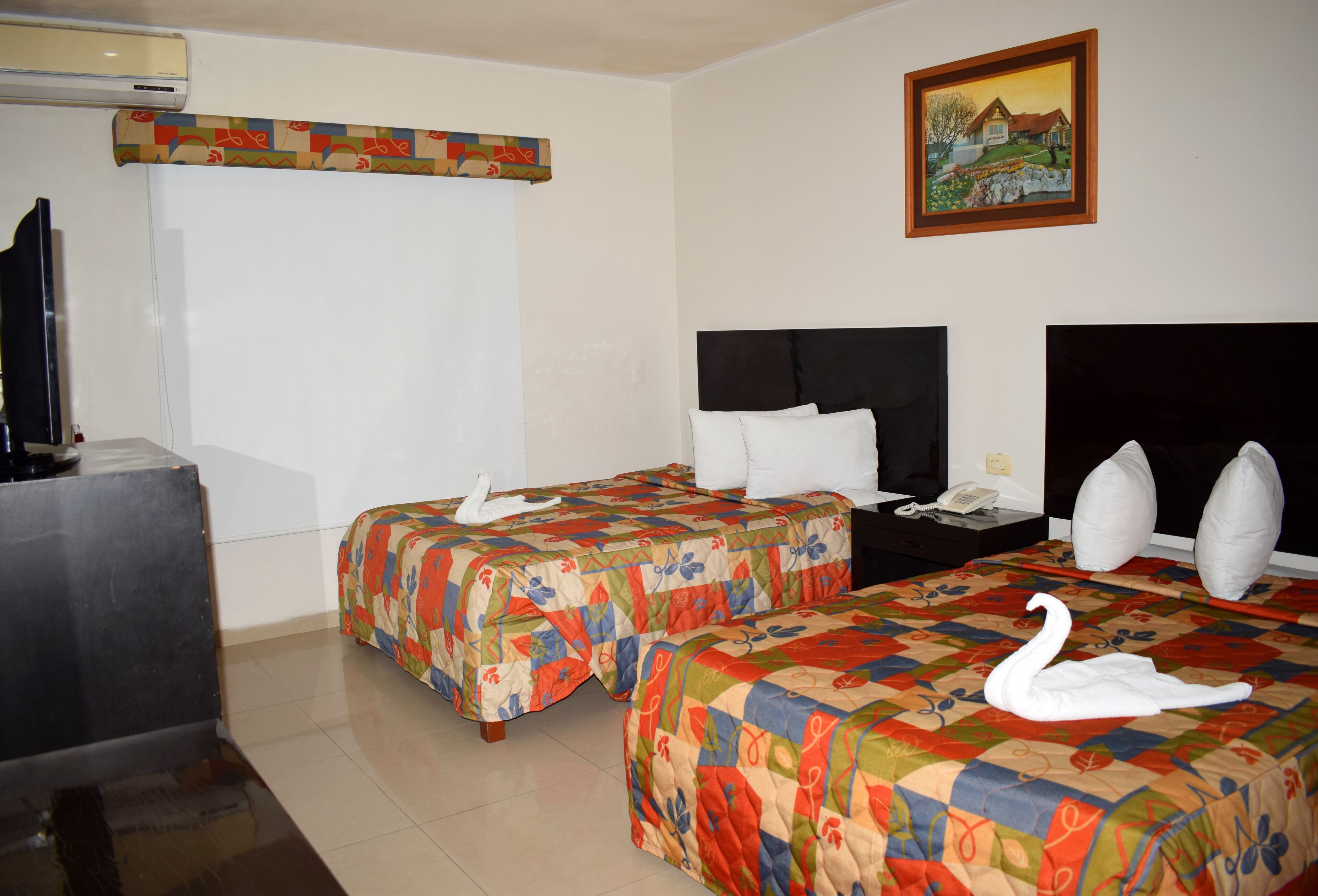 Una habitación de hotel con dos camas, televisión, un cuadro y teléfono en la mesita de noche.